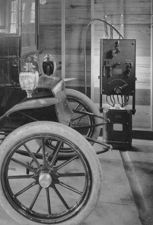 noodoe blog - A black and white photo shows a thick power panel charger connected to a 1910s automobile.