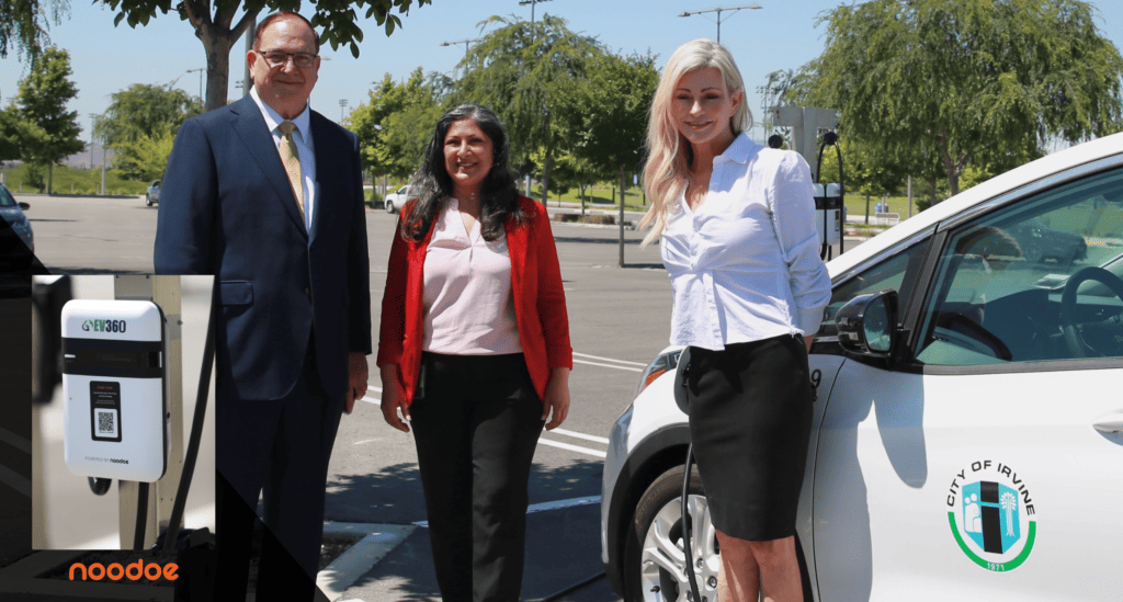 Three smiling individuals stand between a branded smart "Powered by Noodoe" AC charger and electric vehicle with city of Irvine logo.